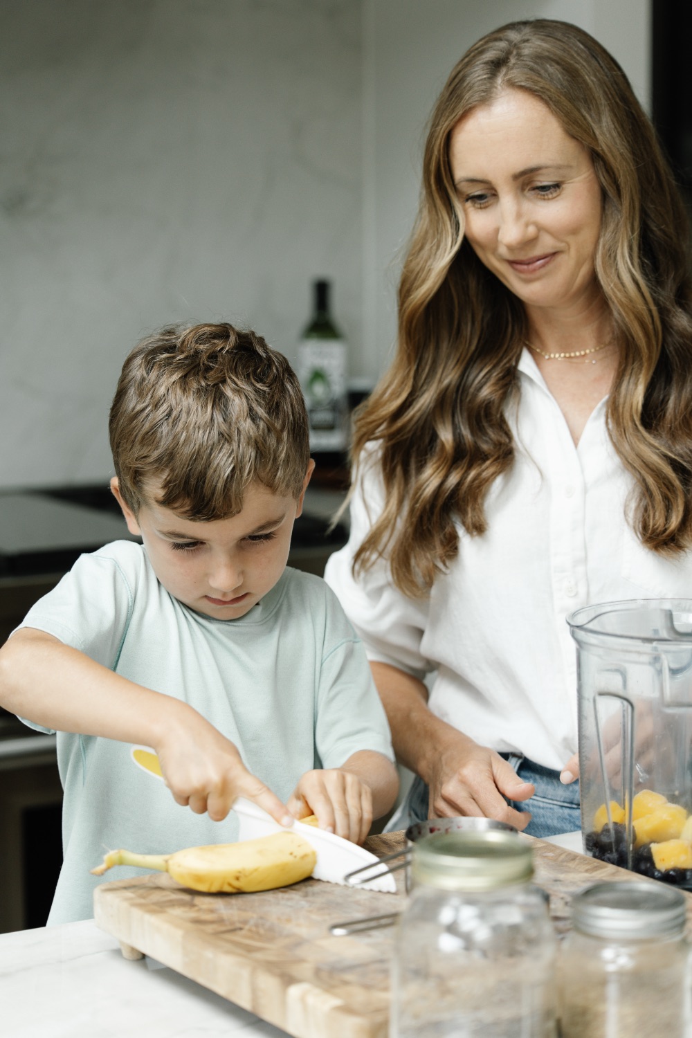 Julia helping a young boy slice a banana in the kitchen