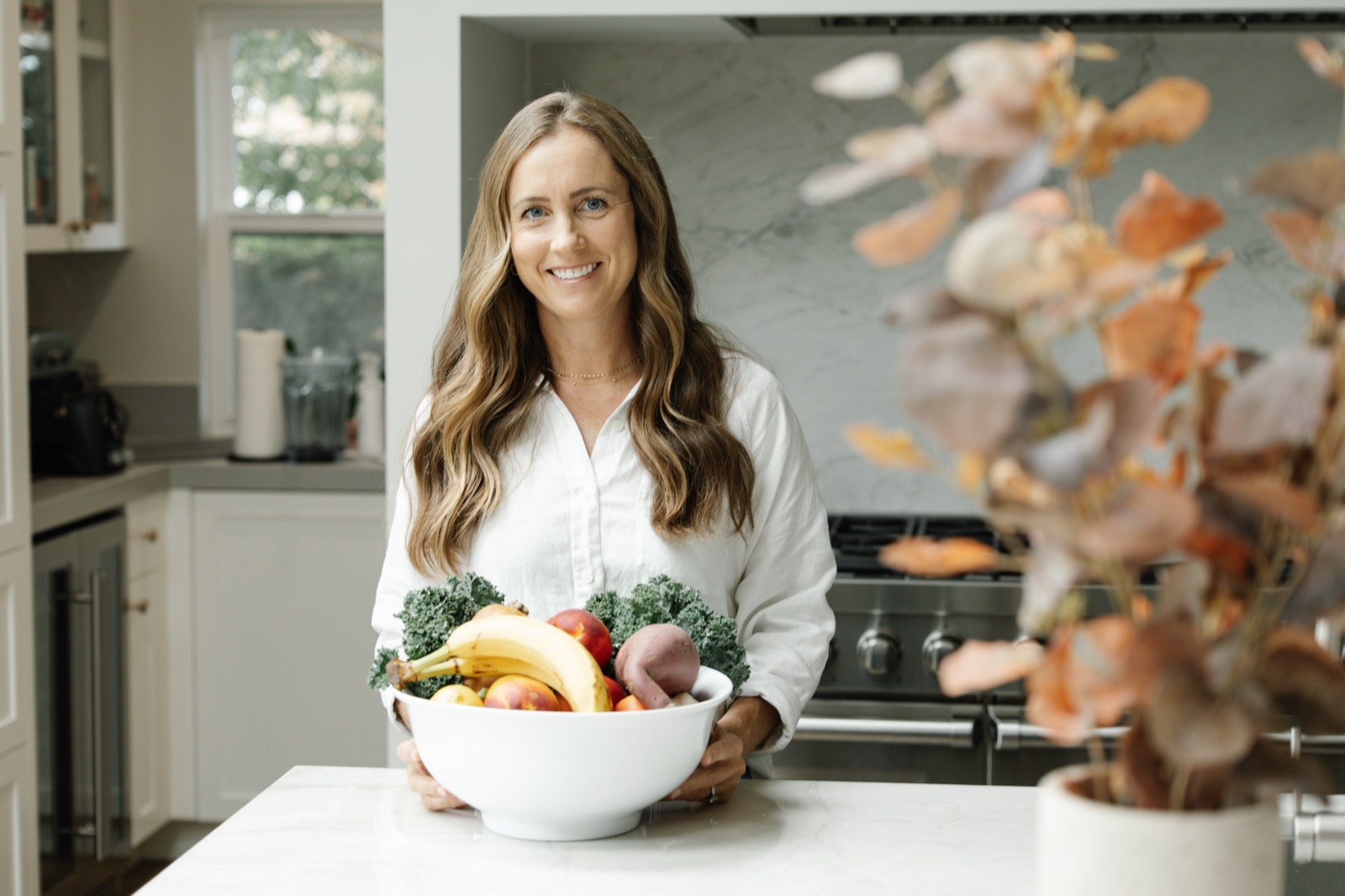 Julia Descalso smiling in her kitchen, holding a bowl of fresh fruit and vegetables